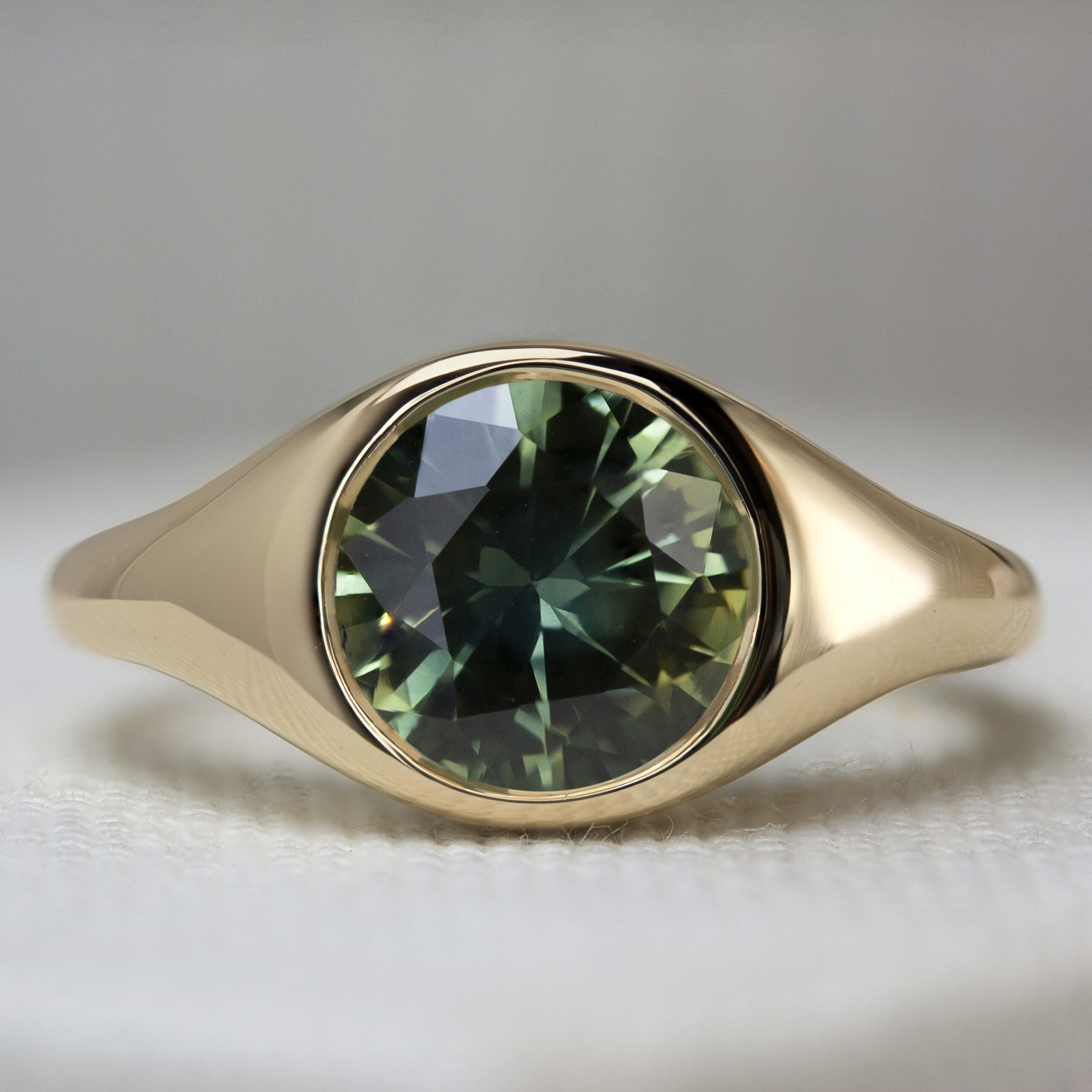 Custom green sapphire round signet ring by Philadelphia's Emily Chelsea Jewelry, featuring soft curves and a flush-set center diamond.