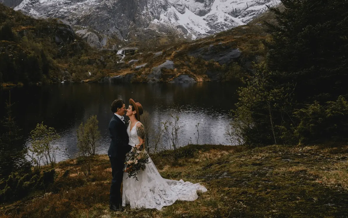 A newlywed couple embrace in front of a forest & lake backdrop