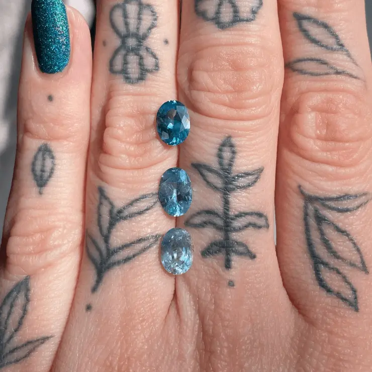 Blue stones sit atop a tattooed hand to demsonstrate the small size